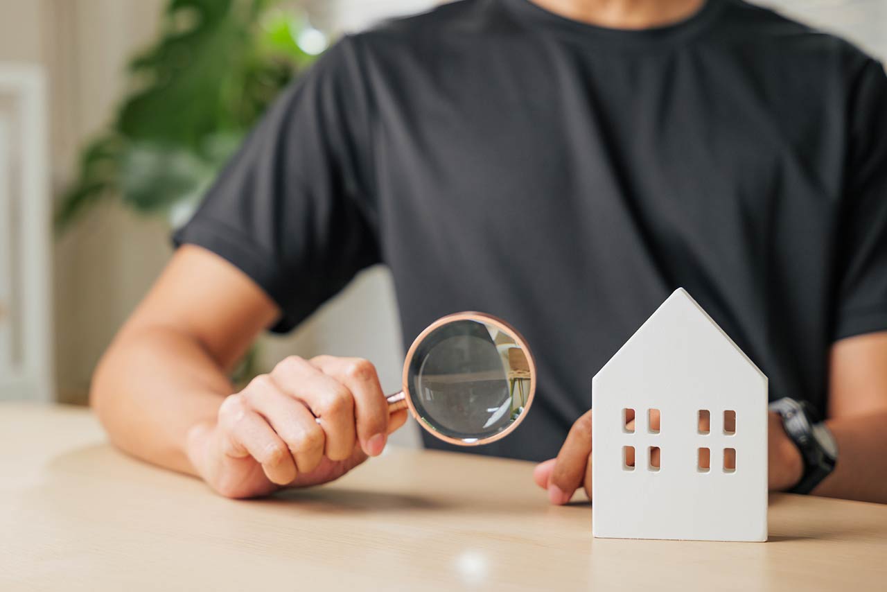 Hand with a magnifying glass examines a block house for real estate purposes