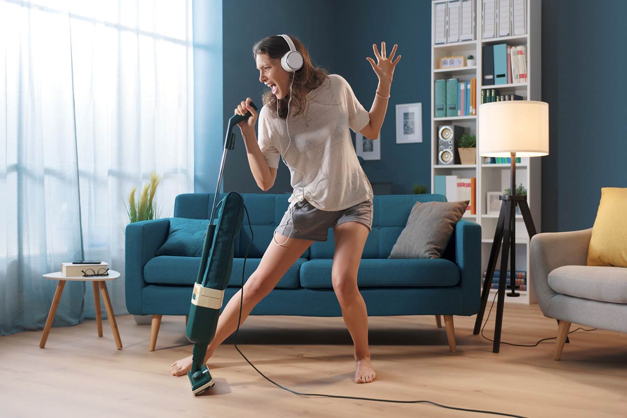 Cheerful woman cleaning up her home and singing, using the vacuum cleaner as a microphone