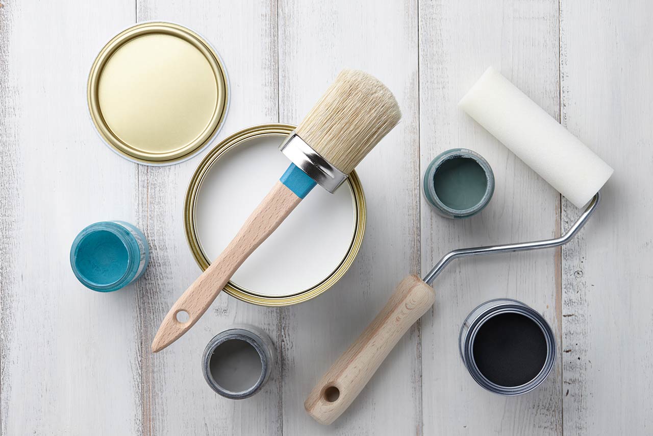 Paint brush, sponge roller, paints, waxes and other painting or decorating supplies on white wooden planks